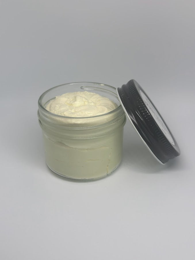 A four ounce glass jar of whipped shea butter with an open lid
